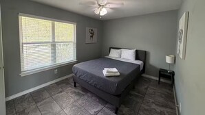 Ein Schlafzimmer mit Bett, Deckenventilator, Fenster mit Jalousien und einem kleinen Nachttisch.
