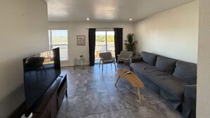 Ein Wohnzimmer mit einer Couch, einem Fernseher, einem Couchtisch und einem Balkon mit Blick.