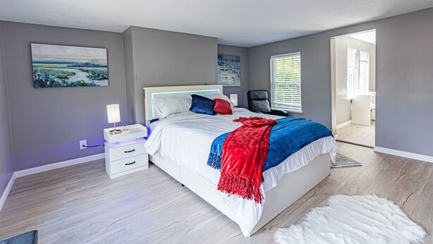 A modern bedroom with a large bed, a nightstand, a chair, and a view of the outdoors. - Spacious Home with Porch Sleeps 6 Near Pitt & UPMC (Pittsburgh)