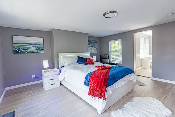 Ein modernes Schlafzimmer mit einem großen Bett, einem Nachttisch, einem Sessel und Blick ins Freie.