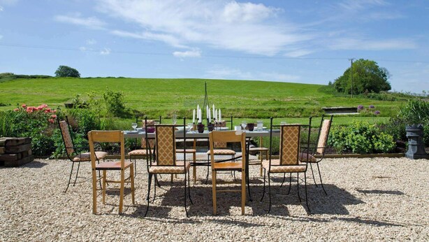 Ein Tisch im Freien mit Stühlen, Blick auf ein grünes Feld und einen klaren Himmel.