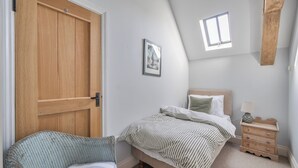 Ein Schlafzimmer mit Bett, Stuhl, Nachttisch, Fenster und Tür.