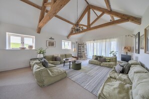 Ein geräumiges Wohnzimmer mit hohen Decken, einer Chandelüster, mehreren Sitzgelegenheiten und großen Fenstern.