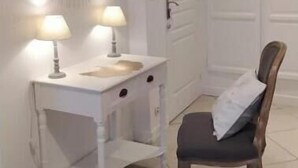 A room with a white vanity, two lamps, a mirror, a wooden chair, and a door.