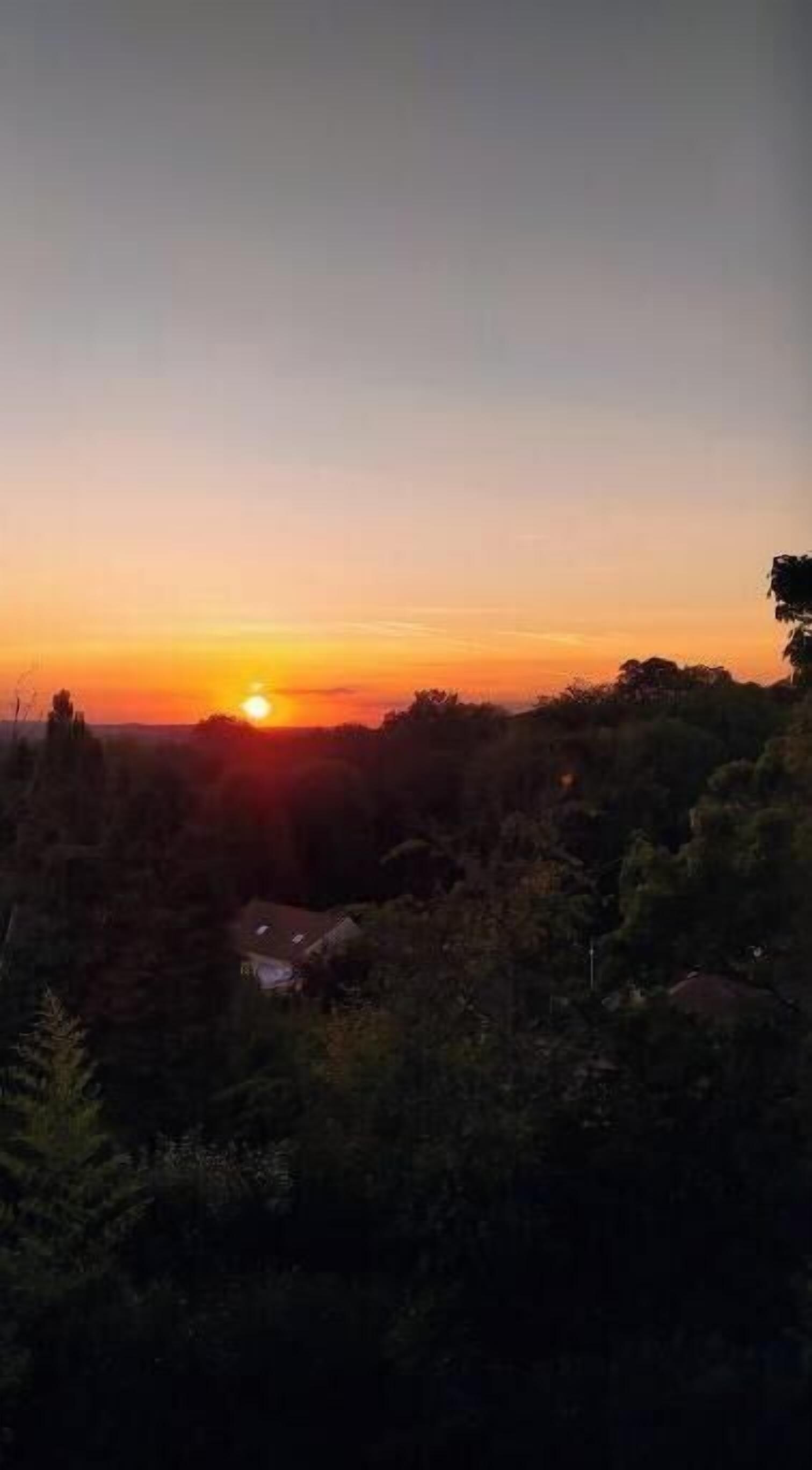A sunset over a landscape with trees and a small building.