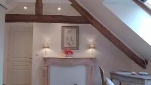 A room with a sloped ceiling, a fireplace, a wooden chair, and a desk.