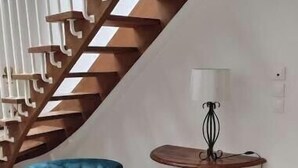 A staircase with wooden railings, two blue upholstered chairs with wooden legs, a small round table with a lamp, and a white furry rug on the floor.