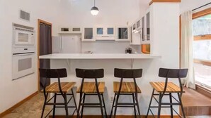 A compact kitchen with a central island, three wooden chairs, and a window with curtains. - Quirky & Fun 4 Bedroom Home in Travis Heights (Austin)