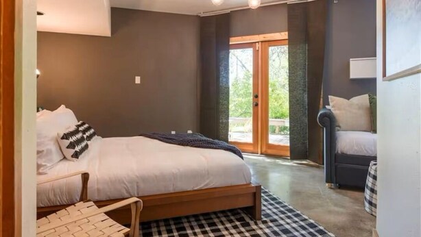 A bedroom with a bed, a chair, a checkered rug, and a view of the outdoors. - Quirky & Fun 4 Bedroom Home in Travis Heights (Austin)