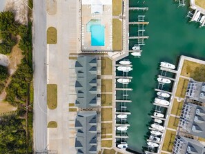 Vue aérienne d’une marina avec des bateaux amarrés, une piscine et des bâtiments adjacents.