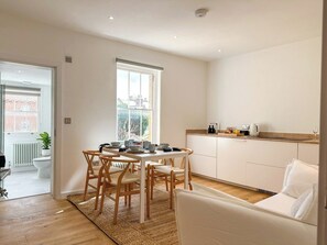 A modern kitchen with white cabinets, a dining table with chairs, and a view through the window. - New | Luxury City Centre Oasis | Private Parking (Canterbury)