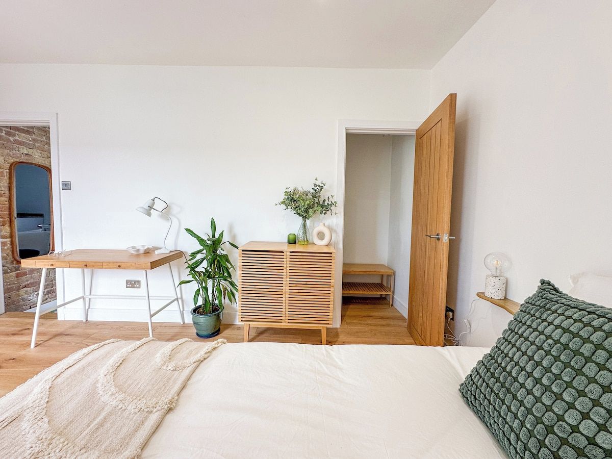 A bedroom with a bed, a desk, a wardrobe, a potted plant, and a bench.