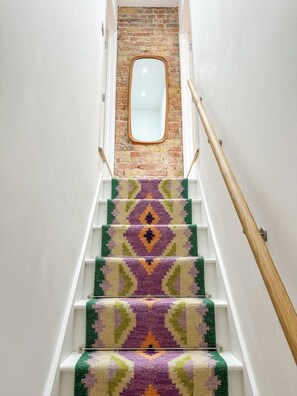A staircase with a patterned carpet, a wooden handrail, and a brick wall with a mirror at the top. - New | Luxury City Centre Oasis | Private Parking (Canterbury)