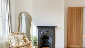 Une pièce avec une cheminée, une porte en bois, un fauteuil en osier et un miroir.