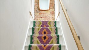 Un escalier recouvert d’une moquette à motifs, doté d’une main courante en bois et bordé d’un mur en briques sur lequel est placé un miroir en haut.