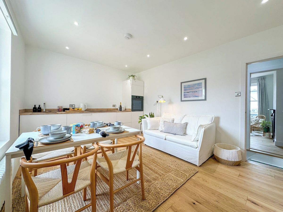 A modern living room with a white sofa, wooden dining table, and chairs.