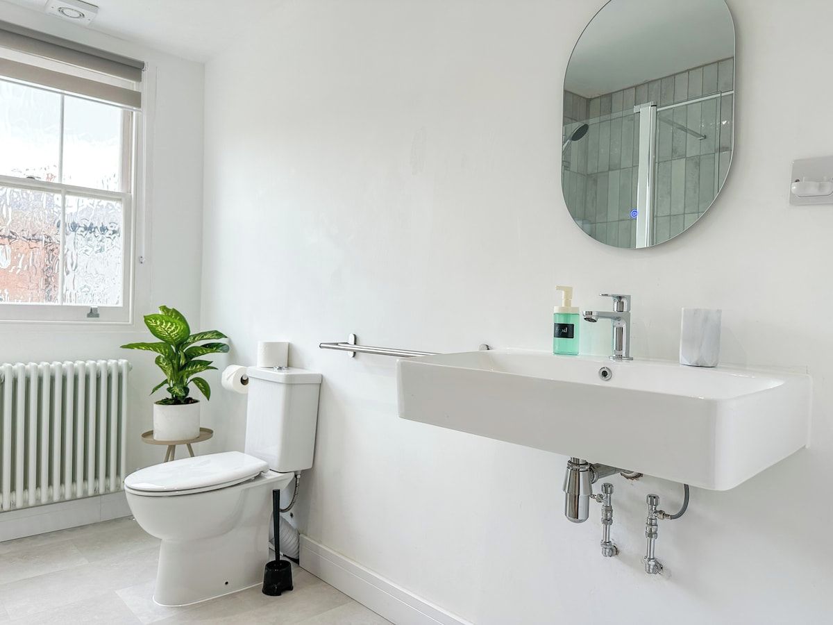 A modern bathroom with a white toilet, a sink with a mirror above it, and a potted plant.