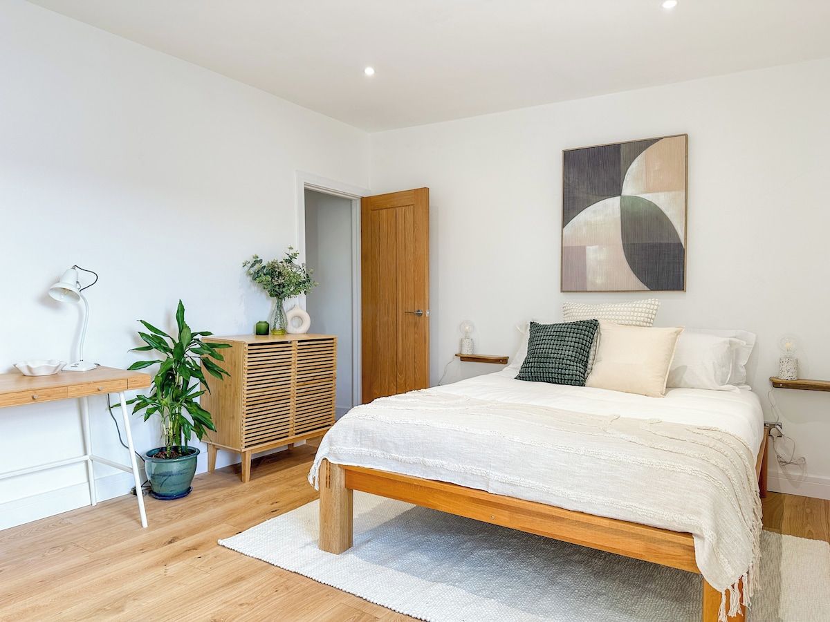 A bedroom with a wooden bed, a desk with a lamp, a potted plant, and a wardrobe.