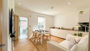 Un salon moderne comprenant un canapé, un coin repas avec une table et des chaises, un espace cuisine et un téléviseur fixé au mur.