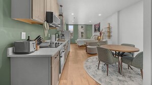 Eine moderne Küche mit einer zentralen Kochinsel, einem Essbereich mit rundem Tisch und Stühlen sowie einem Wohnbereich mit Sofa und Fernseher.