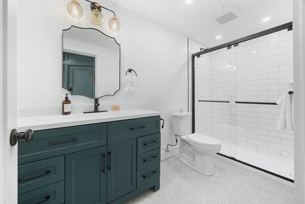 A modern bathroom with a shower enclosure, a toilet, and a vanity with drawers and a mirror.