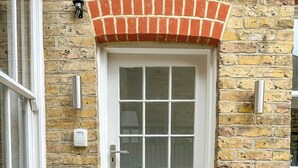 A white door with a brick arch, a window, and two potted plants on the ground.
