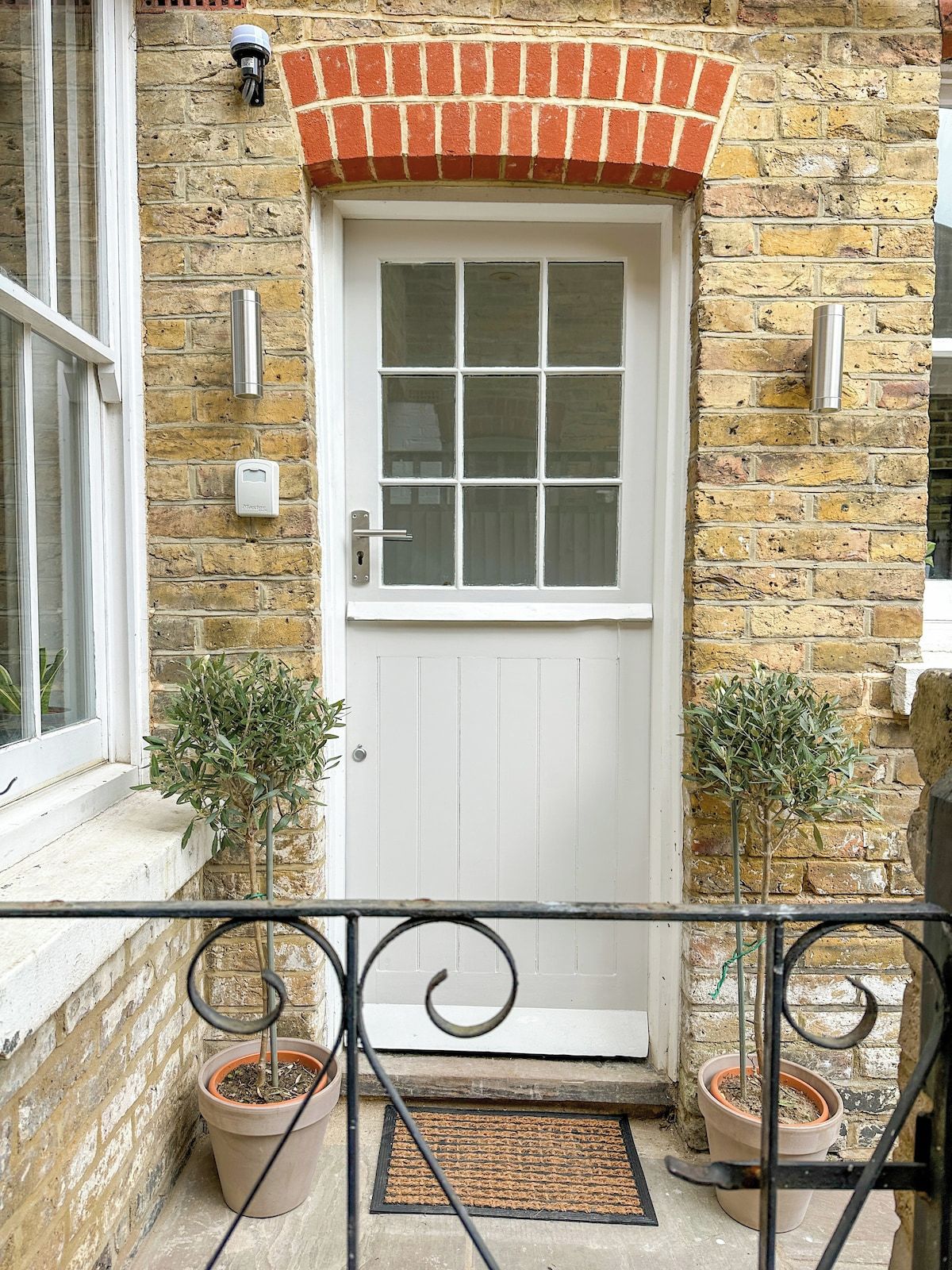 A white door with a brick arch, a window, and two potted plants on the ground.