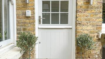 A white door with a brick arch, a window, and two potted plants on the ground.