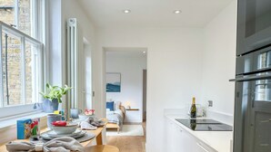 A modern kitchen with white cabinets, a black refrigerator, and a dining area with wooden stools and a table.