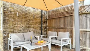 An outdoor seating area with a brick wall, wooden fence, and a large umbrella providing shade.