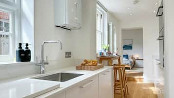 Una cocina moderna con encimera blanca, pileta de acero inoxidable y ventana sobre la pileta.