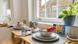 A dining table with plates, a bowl, a spoon, a knife, a box, and a potted plant.