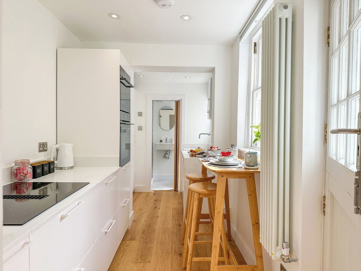 Una cocina moderna con armarios blancos, una placa de inducción negra y un taburete de madera.