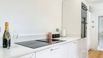 Ett modernt kök med en inbyggd spis, vita köksskåp, en kaffebryggare och en vinflaska.