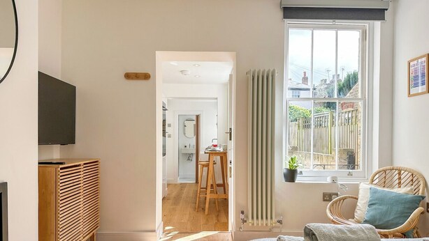 A bedroom with a bed, a TV, a radiator, a window with a view, and a door leading to a bathroom.
