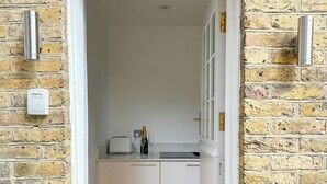 A narrow hallway leading to a kitchen with a brick wall, a white door, and two potted plants.