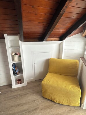 Ein Zimmer mit einem gelben Sofa, weißen Wänden, Holzbalken und einem weißen Schrank mit Regalen.