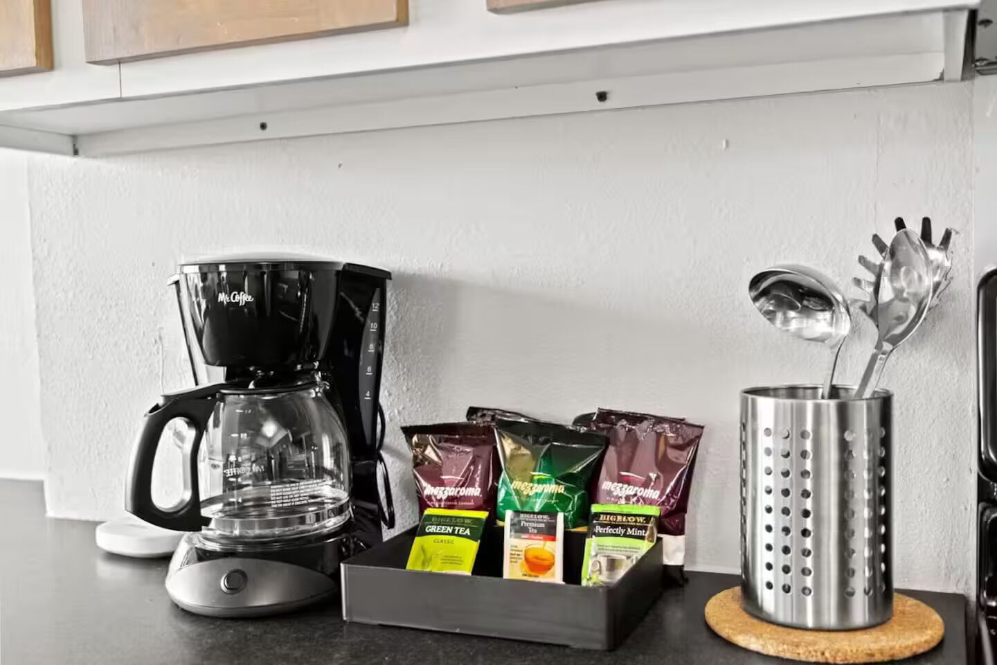 A kitchen counter with a coffee maker, tea packets, and a utensil holder.