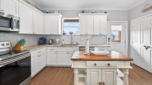 A kitchen with white cabinets, a wooden countertop, a stainless steel oven, and a window with a view. - Steps to the Beach, Stunning Sunrises and Sunsets! (Galveston)