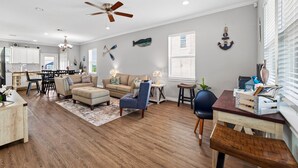 A spacious living area with a dining table, sofas, a ceiling fan, and nautical decor. - Steps to the Beach, Stunning Sunrises and Sunsets! (Galveston)