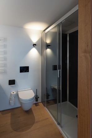 Une salle de bain moderne équipée de toilettes, d’une douche à parois de verre et d’un luminaire fixé au mur.
