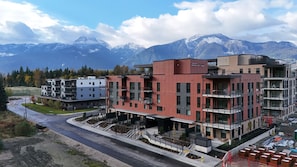 Un immeuble à plusieurs étages doté de balcons, d’un espace de stationnement et surplombant un paysage montagneux.