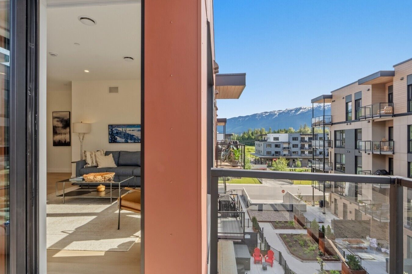 A modern apartment with a balcony, a living room with a sofa and coffee table, and a mountain view.