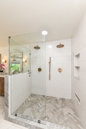 Un bagno moderno con cabina doccia in vetro, pareti piastrellate di bianco e un pavimento a motivi a spina di pesce.