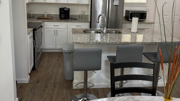 Una cocina moderna con armarios blancos, un refrigerador de acero inoxidable, encimera de granito y una zona de bar con taburetes.