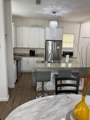 Una cocina moderna con armarios blancos, un refrigerador de acero inoxidable, encimera de granito y una zona de bar con taburetes.