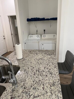 A laundry area with two washing machines, a countertop with a sink, and a chair. - Charming 3-bedroom house with AC in vibrant Atlanta (Atlanta)