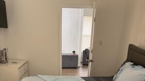 Un dormitorio con una cama, una mesita de noche, una silla y una puerta que da a otra habitación.