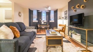 A living room with a sofa, coffee table, TV stand, and a dining area with chairs and a table. - Chic Downtown Denver Retreat | Walk Everywhere + Stylish Comfort (Denver)