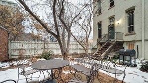 A patio with a round table and metal chairs, a brick wall, a tree, and a building with a staircase. - Chic Downtown Denver Retreat | Walk Everywhere + Stylish Comfort (Denver)